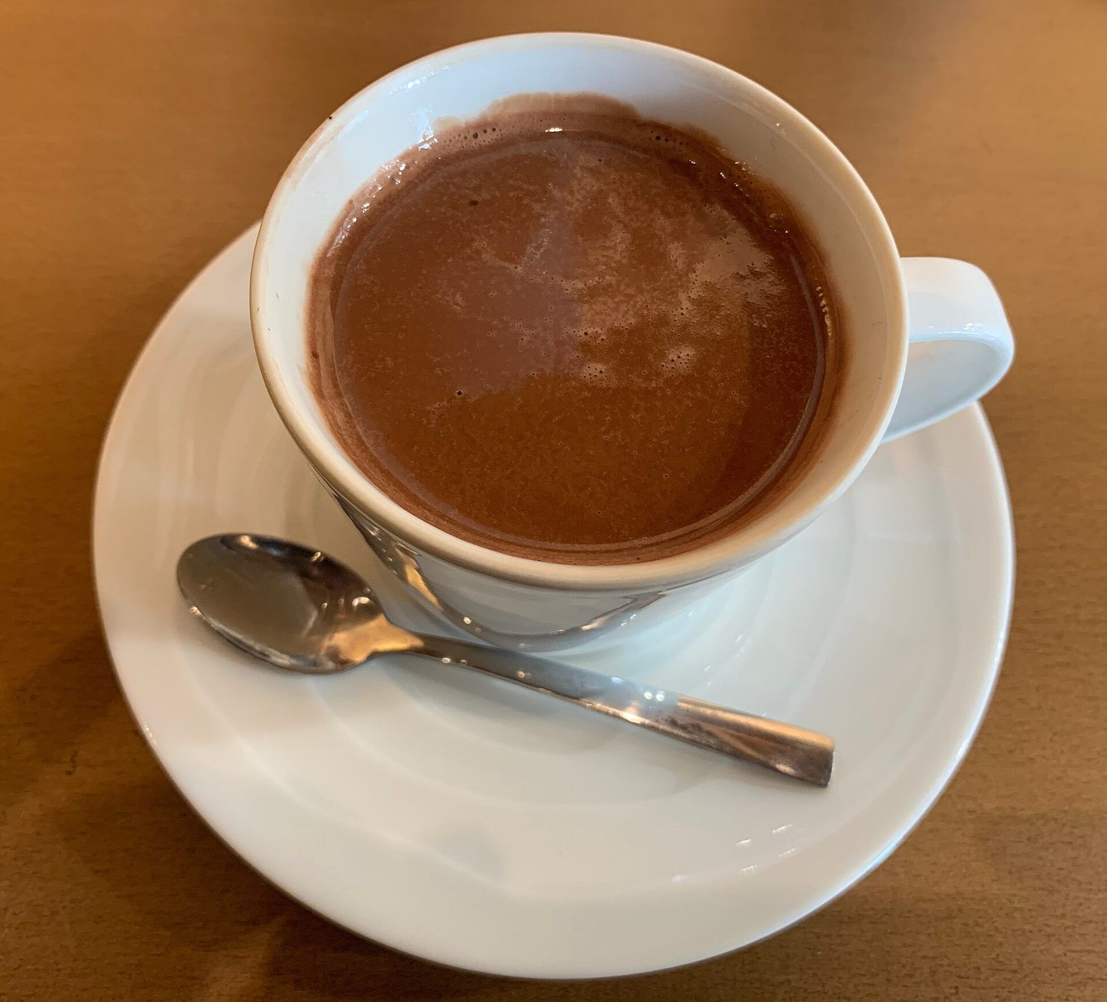 Cup of hot chocolate on a white saucer with a teaspoon
