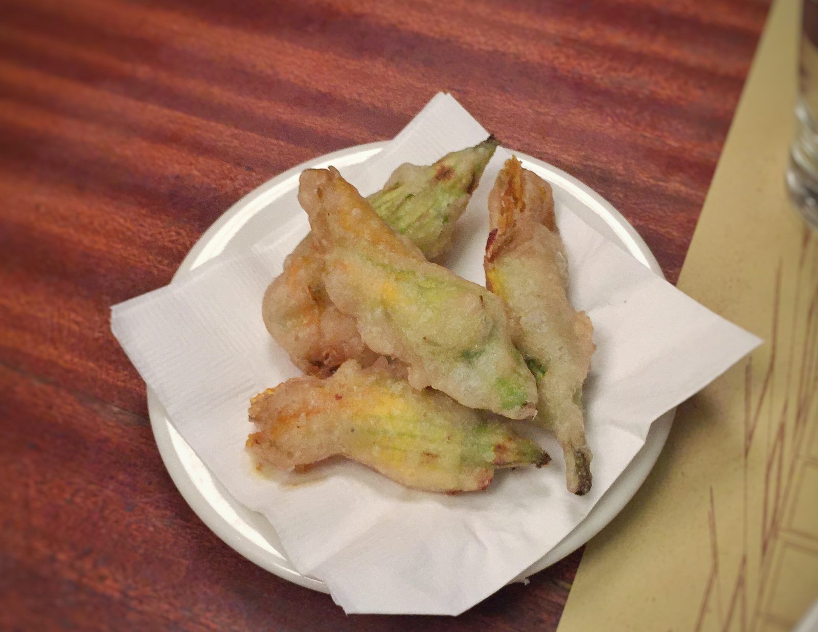 Batter-fried courgette flowers on a small plate lined with a paper napkin