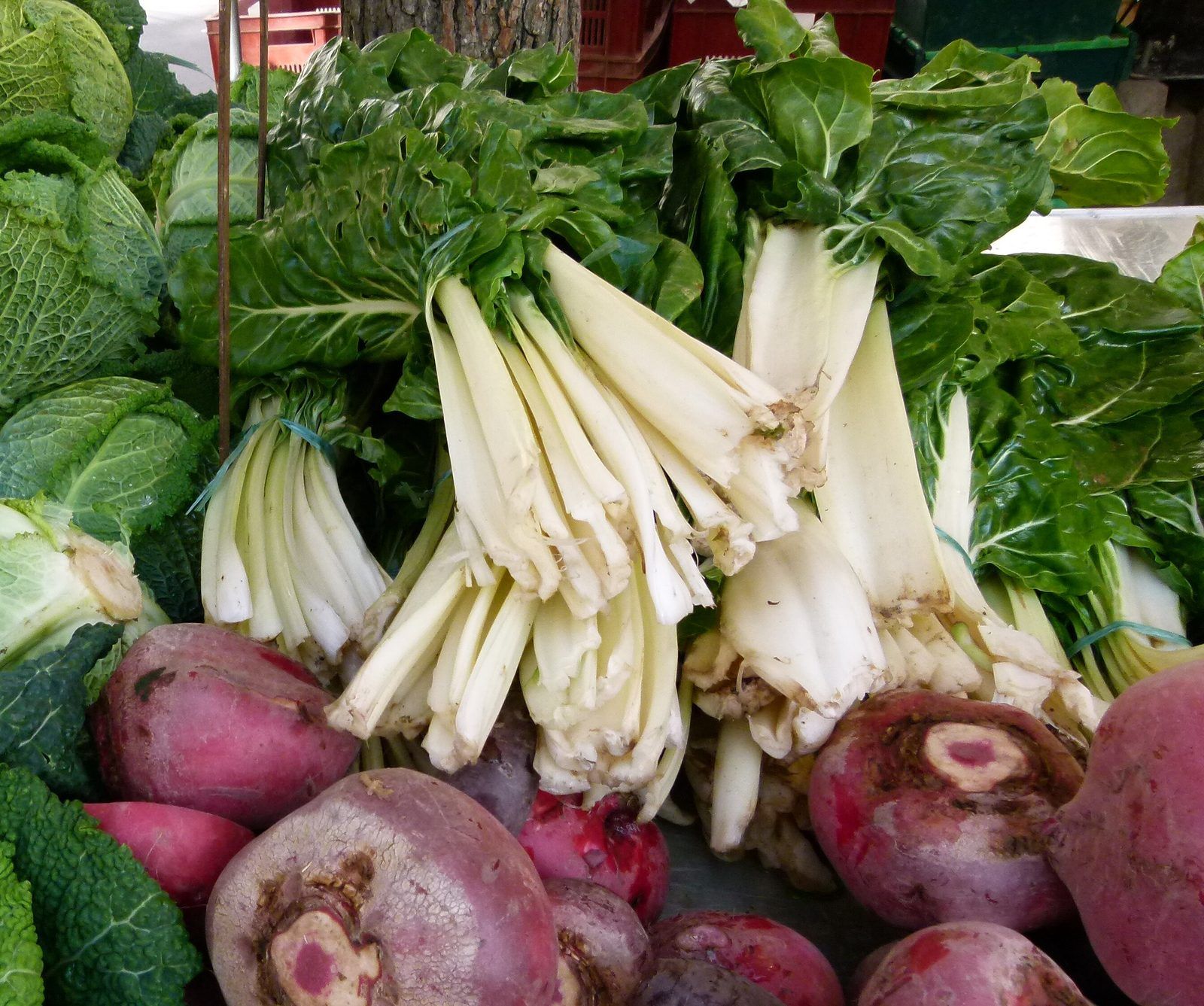 Bunches of white-stemmed Swiss chard on a market stall, with beetroots and savoy cabbage