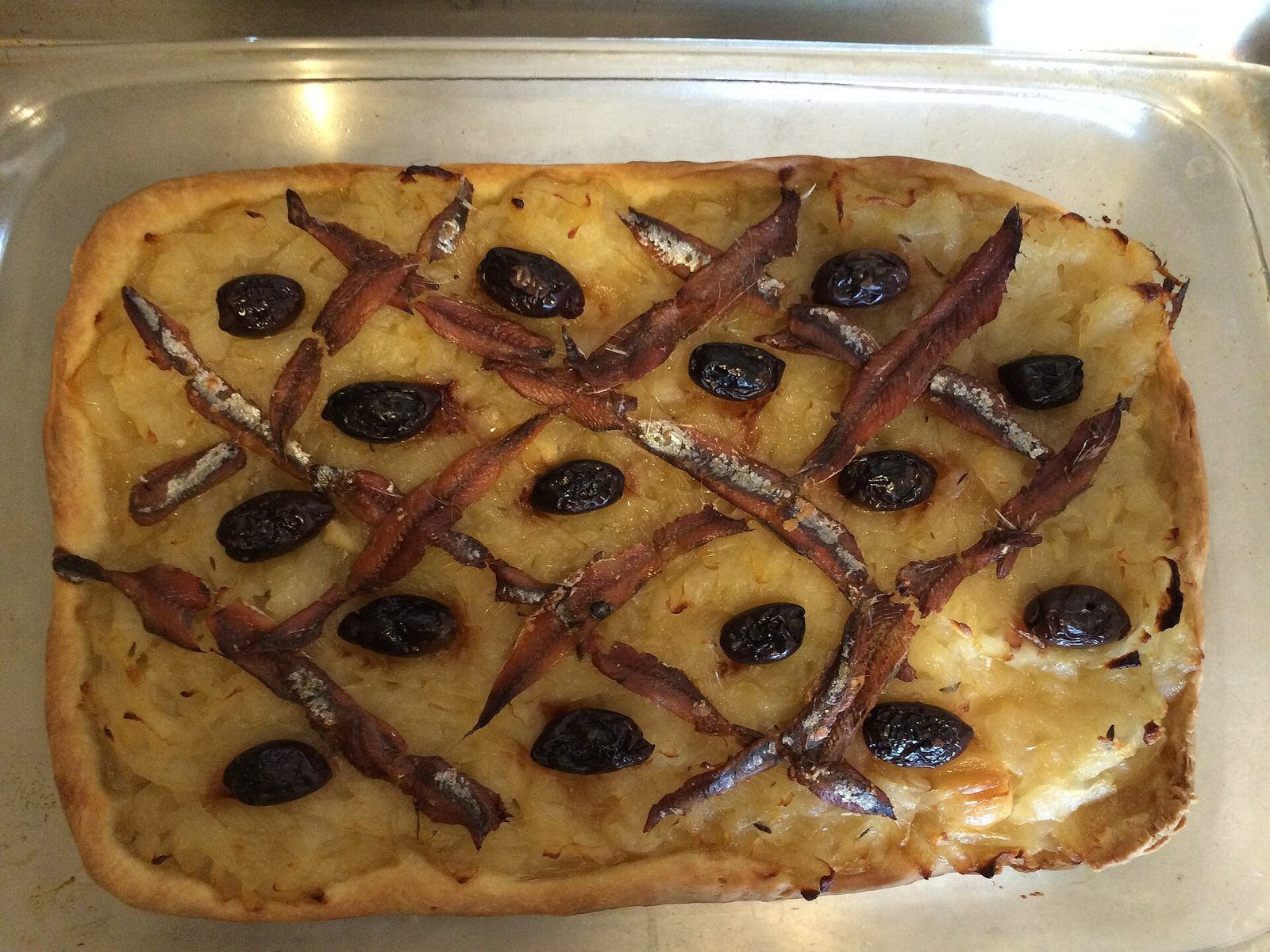 Pissaladière in a baking dish, soft onions under a lattice of anchovies and black olives