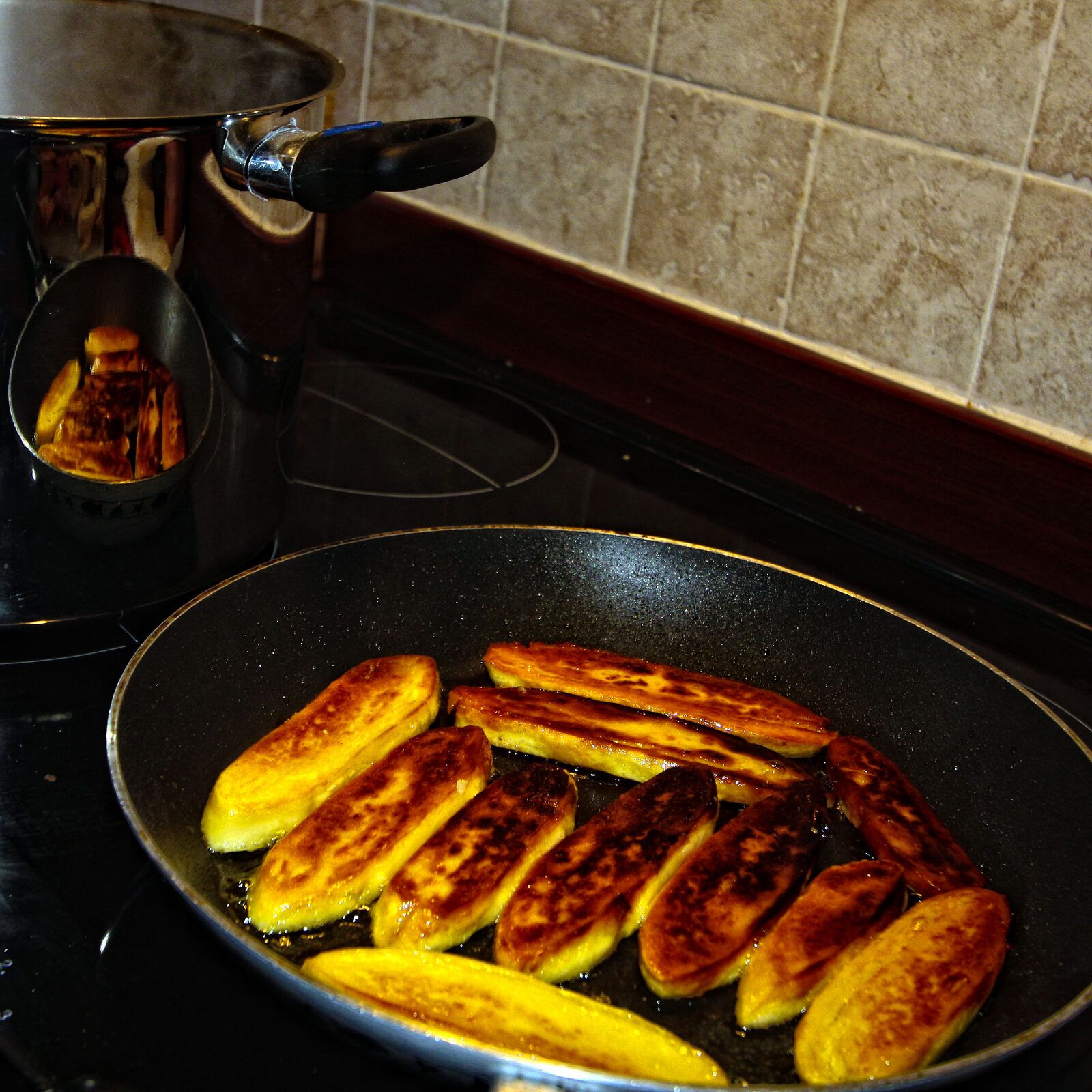 Golden-brown panisse sticks frying in olive oil in a non-stick pan on a hob