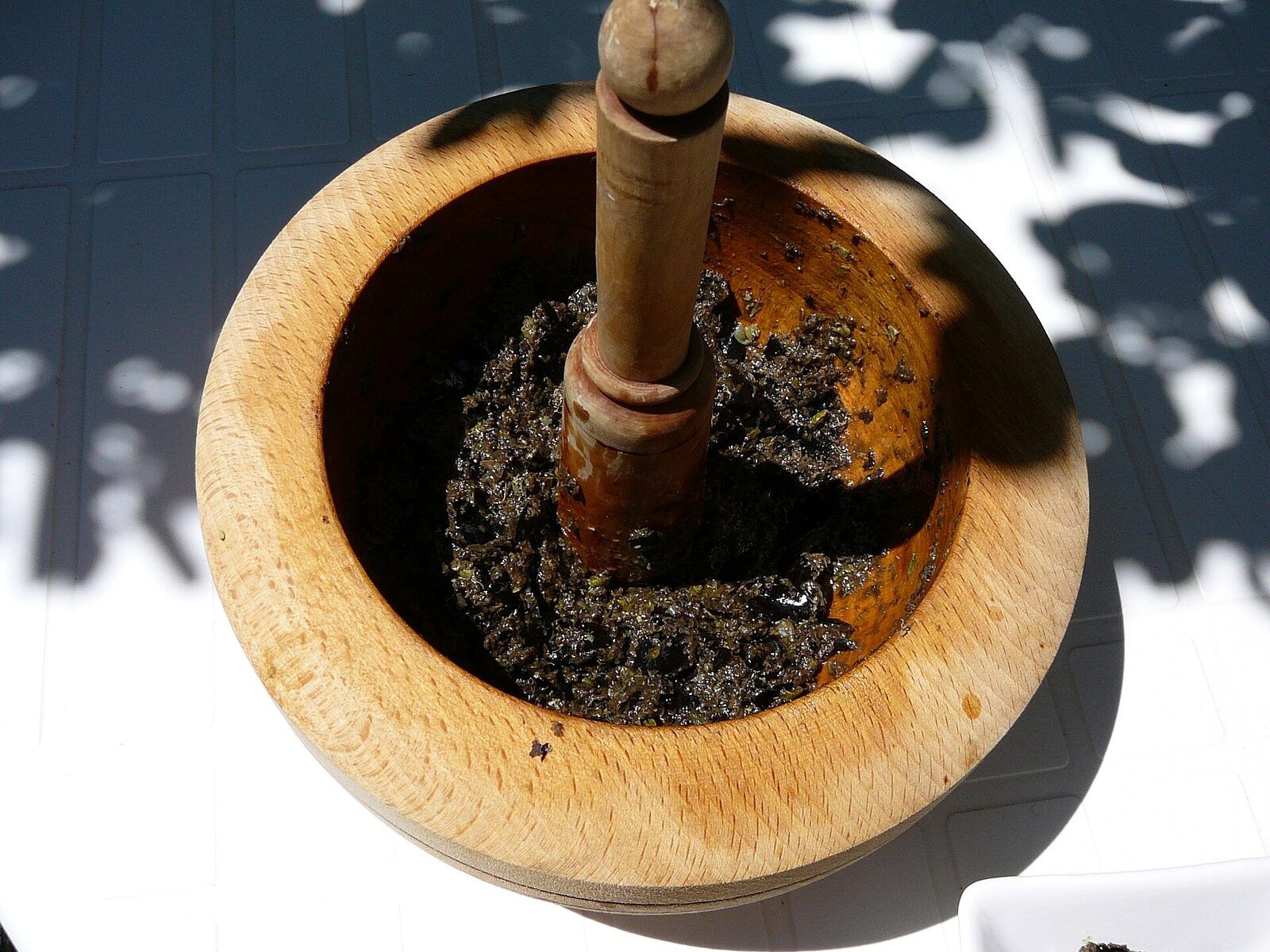 Coarse black tapenade pounded in a wooden mortar with a wooden pestle standing in it