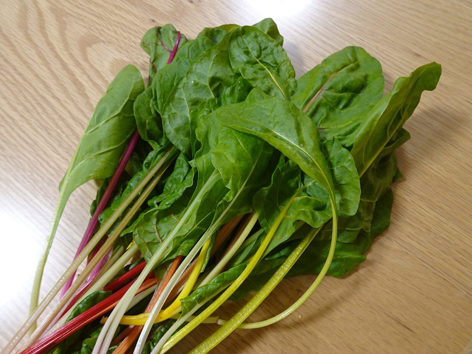 Fresh Swiss chard leaves with thin red, yellow and white ribs, spread on a wooden table