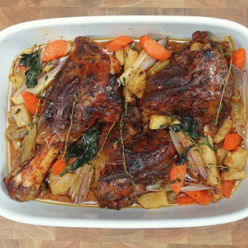 Slow-cooked lamb shank on a rustic plate with tender, juicy meat, surrounded by a rich, savory sauce. Garnished with fresh herbs and served with roasted vegetables for a hearty meal.